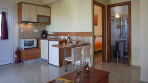 A compact kitchen with a microwave, toaster, and a dining area with chairs and candles. - Cavo Plako Villas (Sitia)