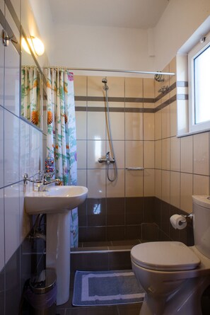 A bathroom with a shower, toilet, sink, and a window.
