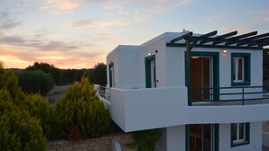 A modern two-story house with a balcony, a stone wall, and a garden. - Cavo Plako Villas (Sitia)