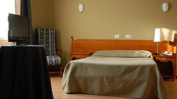 Una habitación de hotel con una cama, un televisor sobre una mesa, una silla y una mesita de noche con una lámpara.