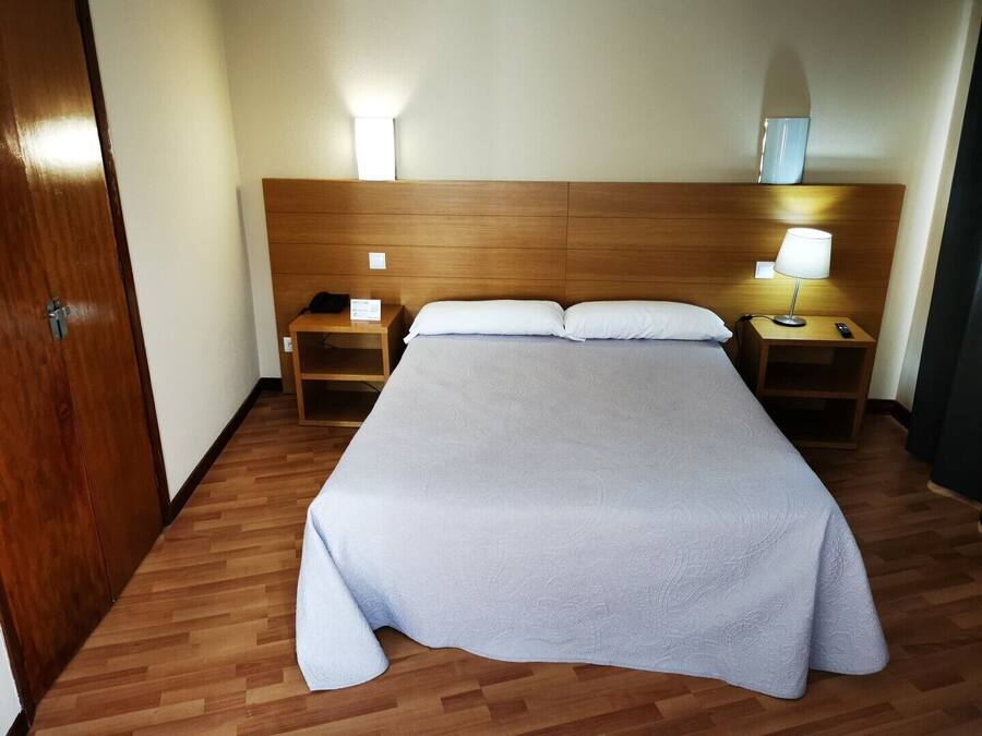 A hotel room with a large bed, wooden headboard, two bedside tables with lamps, and a door.