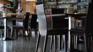 A bar area with multiple tables and chairs, shelves with bottles, and a counter.