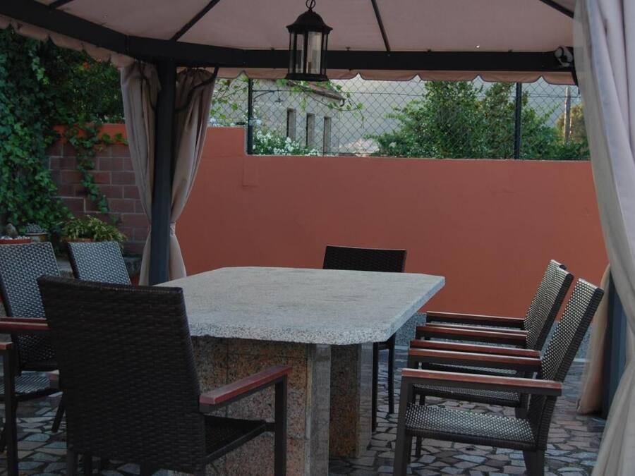 Une terrasse extérieure avec une table en pierre et des chaises en osier, entourée d’un mur de briques et de verdure.