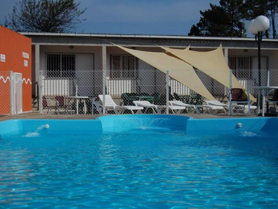 Une piscine dotée de chaises longues et d’un espace ombragé, entourée d’une clôture et bordée d’un bâtiment sur lequel est accrochée une bouée de sauvetage.