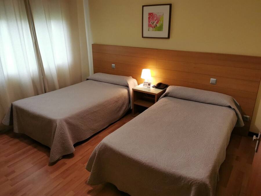 Una camera d'albergo con due letti singoli, un comodino con una lampada e un quadro appeso al muro.