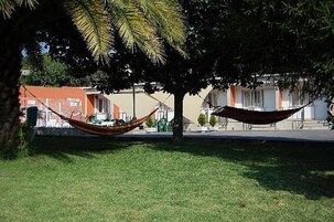 Una hamaca debajo de un árbol en un área con césped y edificios al fondo.