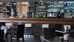 A bar area with shelves of various liquor bottles, a coffee machine, and bar stools.