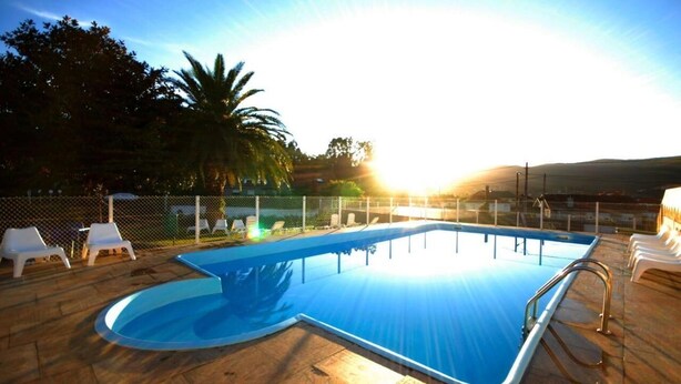A swimming pool with a curved edge, surrounded by lounge chairs and a fence.
