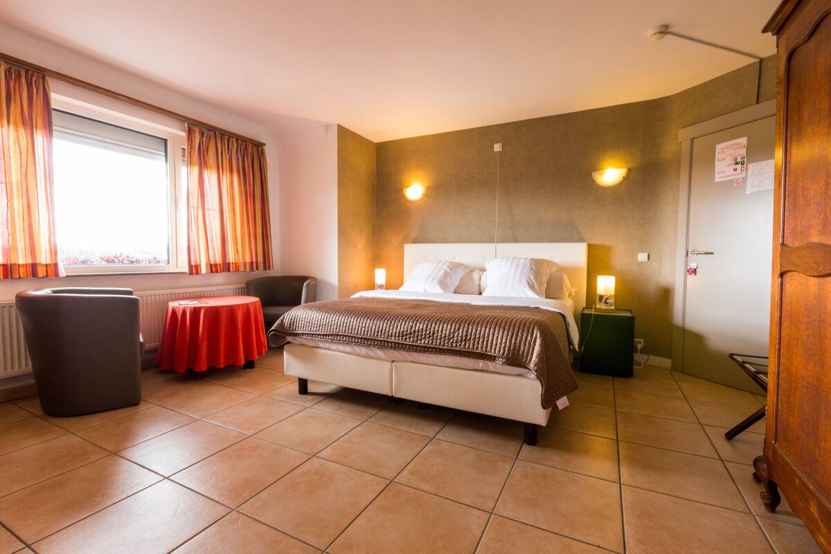 Ein Hotelzimmer mit Bett, einem kleinen Tisch, einem Stuhl und einem Fenster mit Vorhängen.