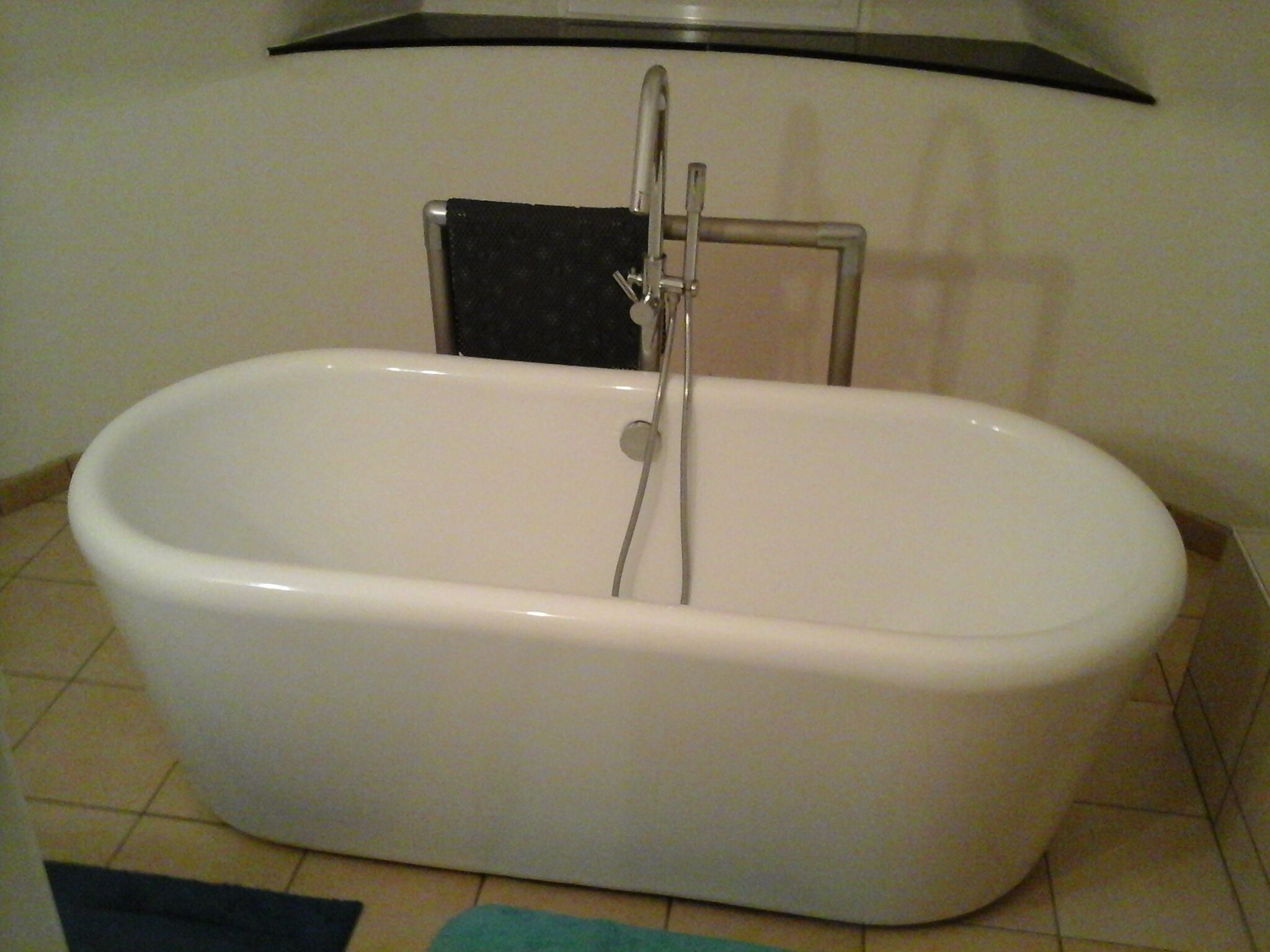 A white freestanding bathtub with a chrome faucet and a black towel rack mounted on the wall.
