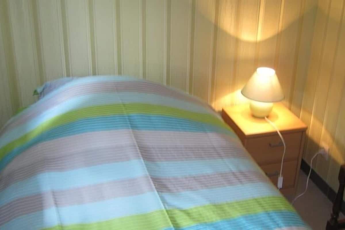 Ein Bett mit einer gestreiften Decke, ein Nachttisch mit einer Lampe und ein Holznachtkästchen.