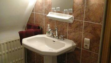 Un baño con lavamanos pedestal, espejo, toallero y cubo de basura.