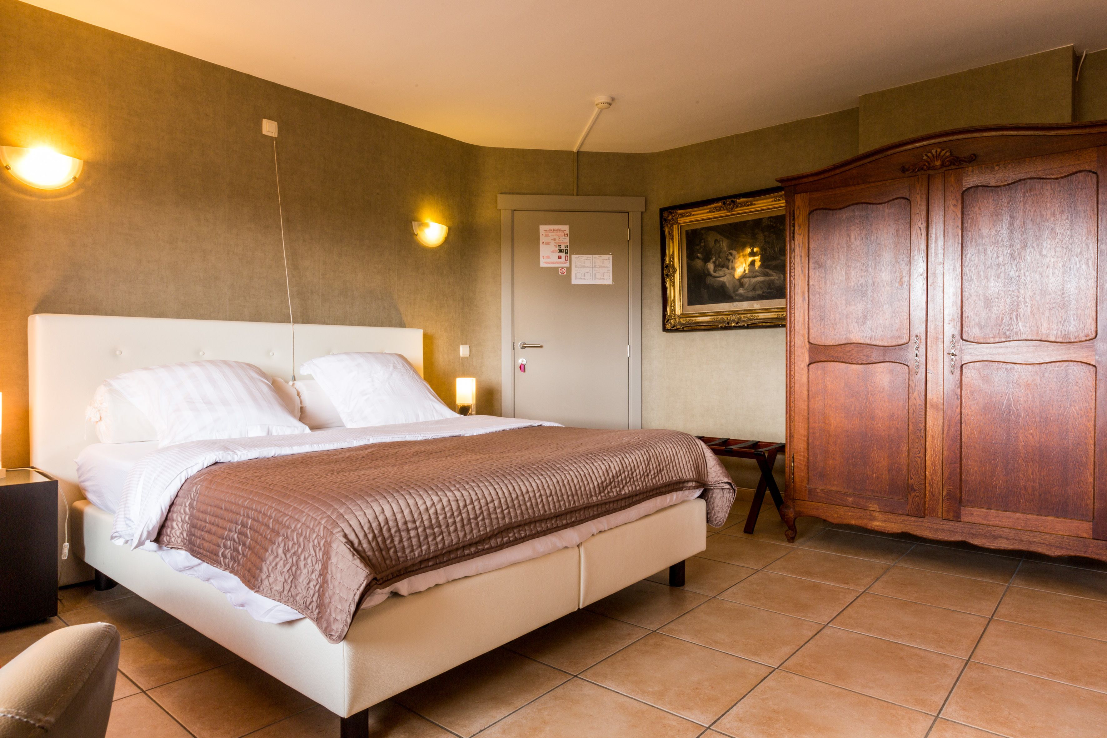Une chambre d’hôtel comprenant un lit, une table de chevet, une lampe, une armoire et une porte sur laquelle est affiché un avis.