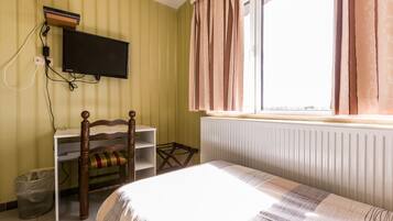 A room with a bed, a desk with a chair, a television mounted on the wall, and a window with curtains.