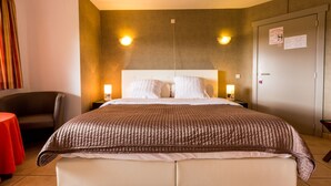 Een hotelkamer met een groot bed, twee nachtkastjes met lampen, een stoel en een rode tafel.