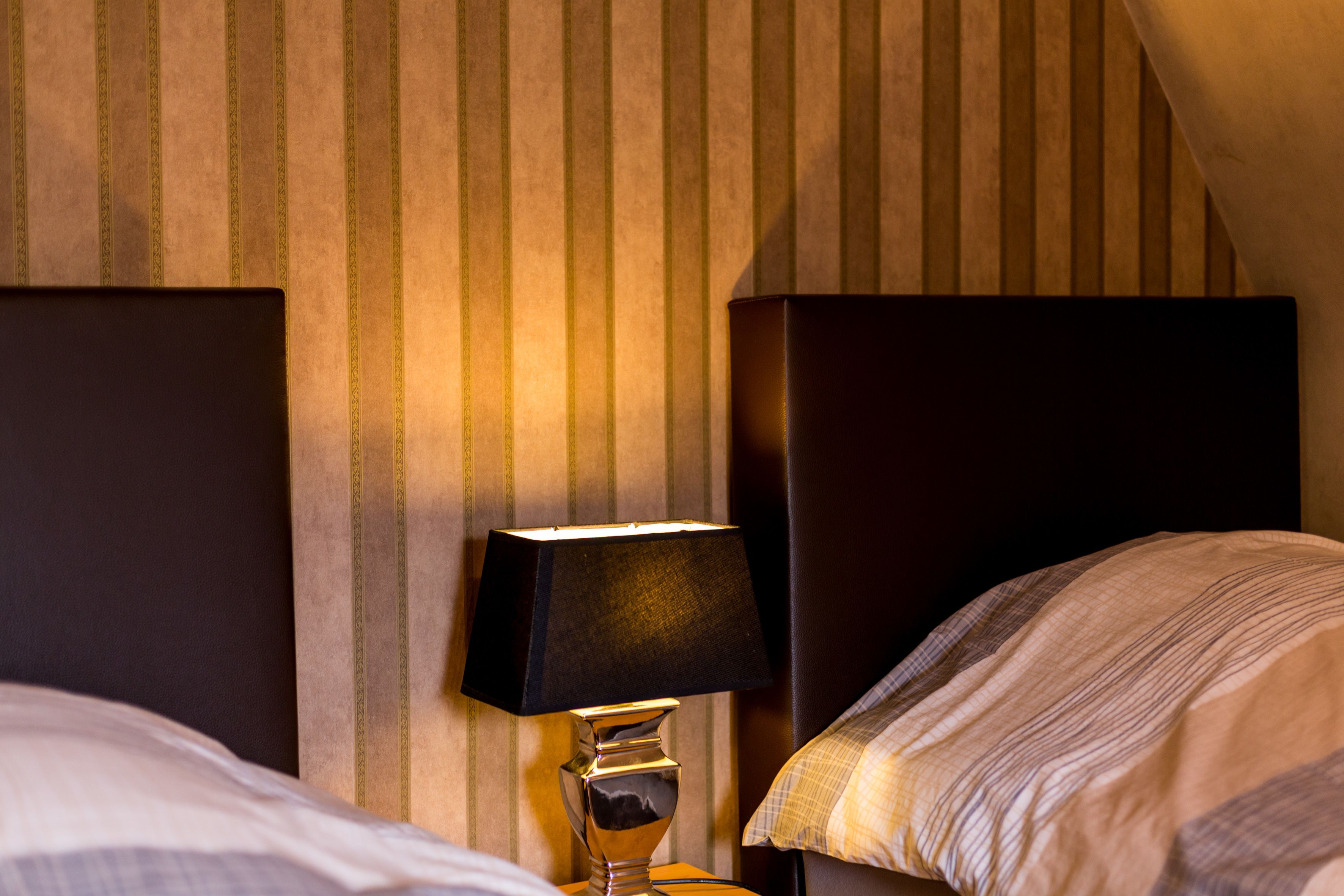 A hotel room with a striped wallpaper, a bedside lamp, and a bed with a striped bedspread.