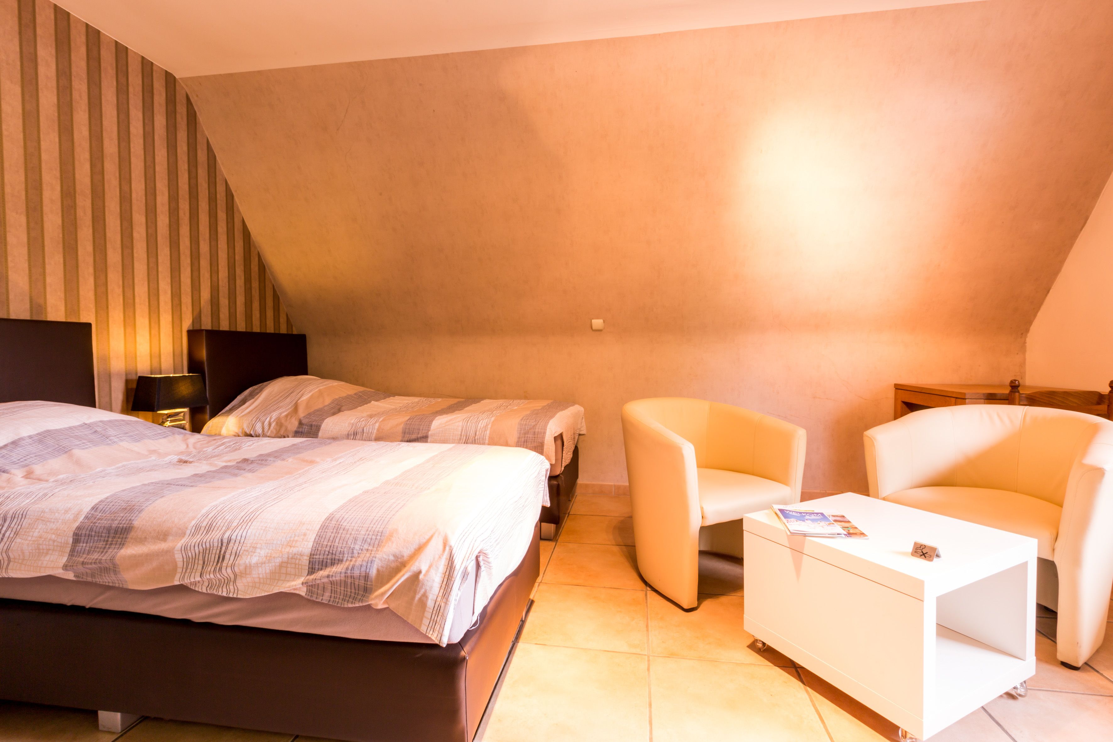 Un dormitorio con dos camas, una mesita de noche blanca, una silla y una lámpara.