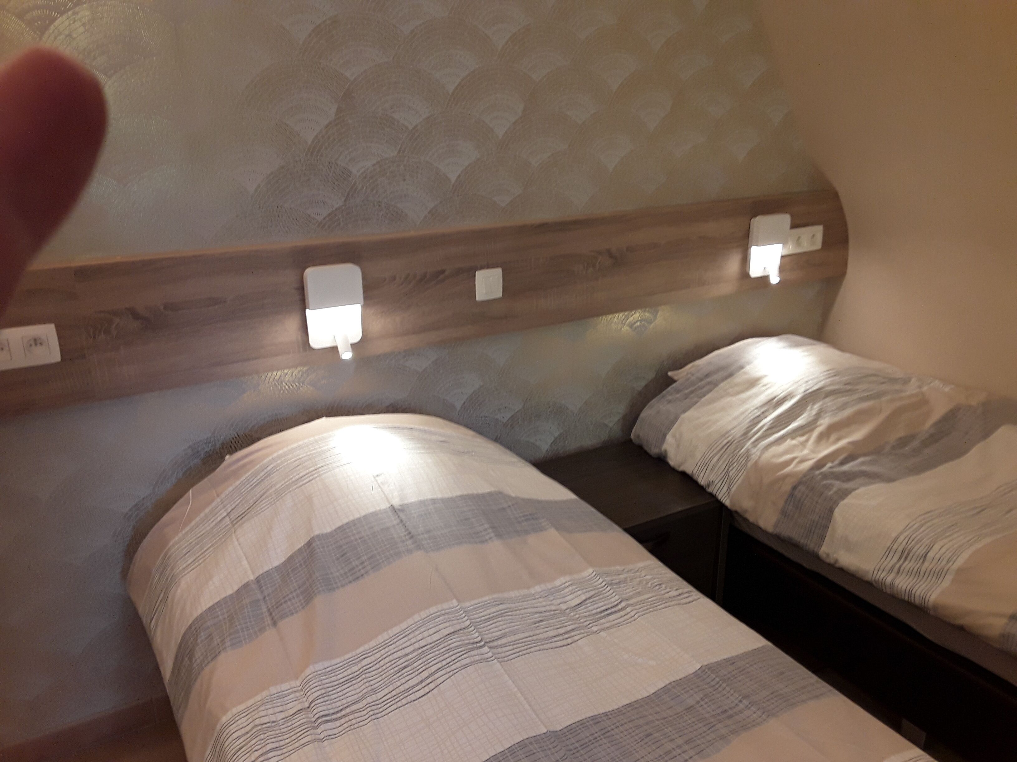 Una habitación con dos camas, cada una con ropa de cama a rayas. Hay luminarias fijadas en la pared sobre las camas.