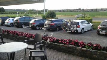Uma área de estacionamento com vários carros e uma bicicleta. Há mesas e cadeiras ao ar livre.