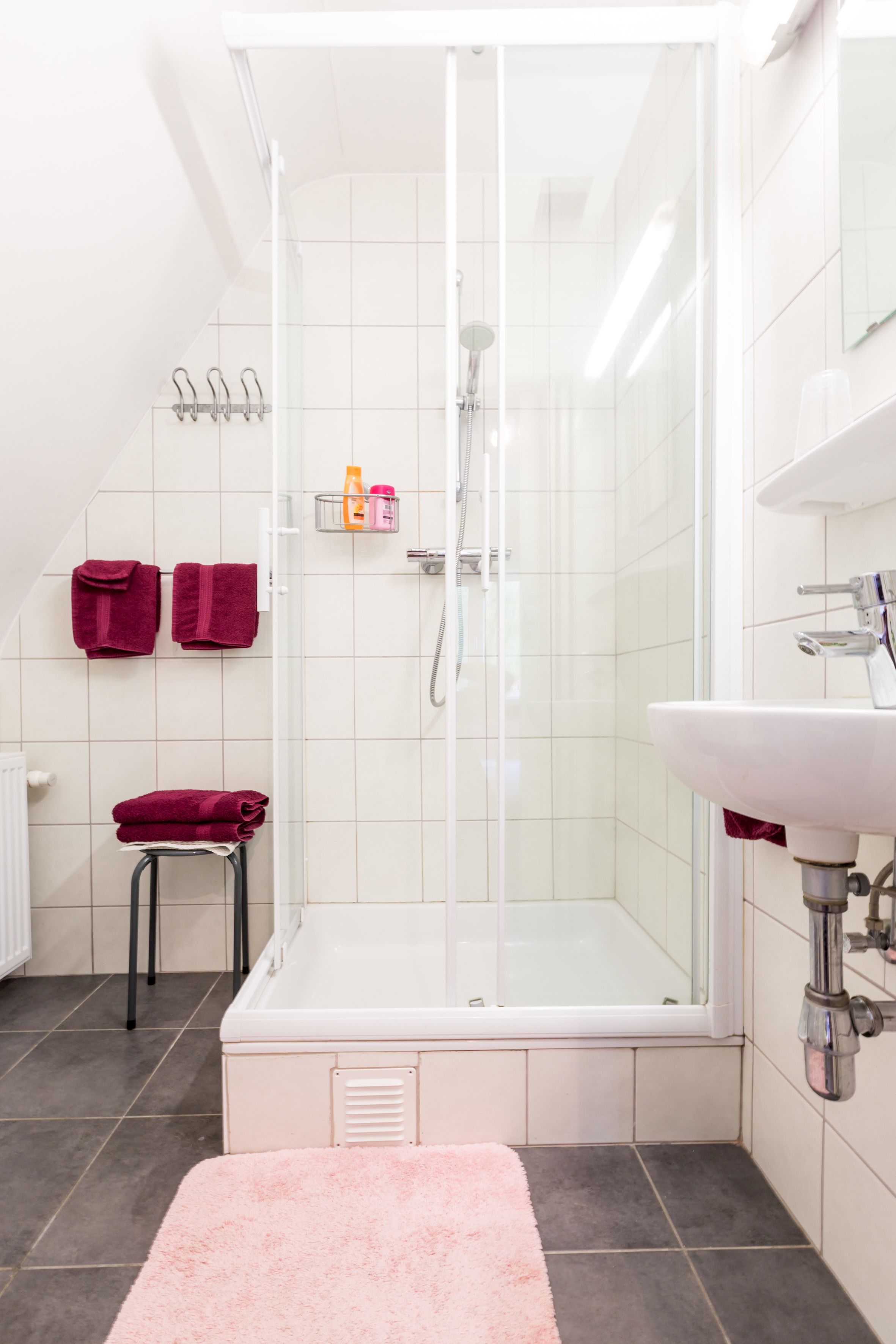 Uma casa de banho moderna com cabine de duche em vidro, lavatório branco e toalha rosa no chão.