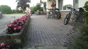 Een geplaveid pad met bloembedden, fietsen en terrasstoelen.