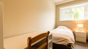 A bedroom with a bed, a bedside table, a chair, and a window with daylight.