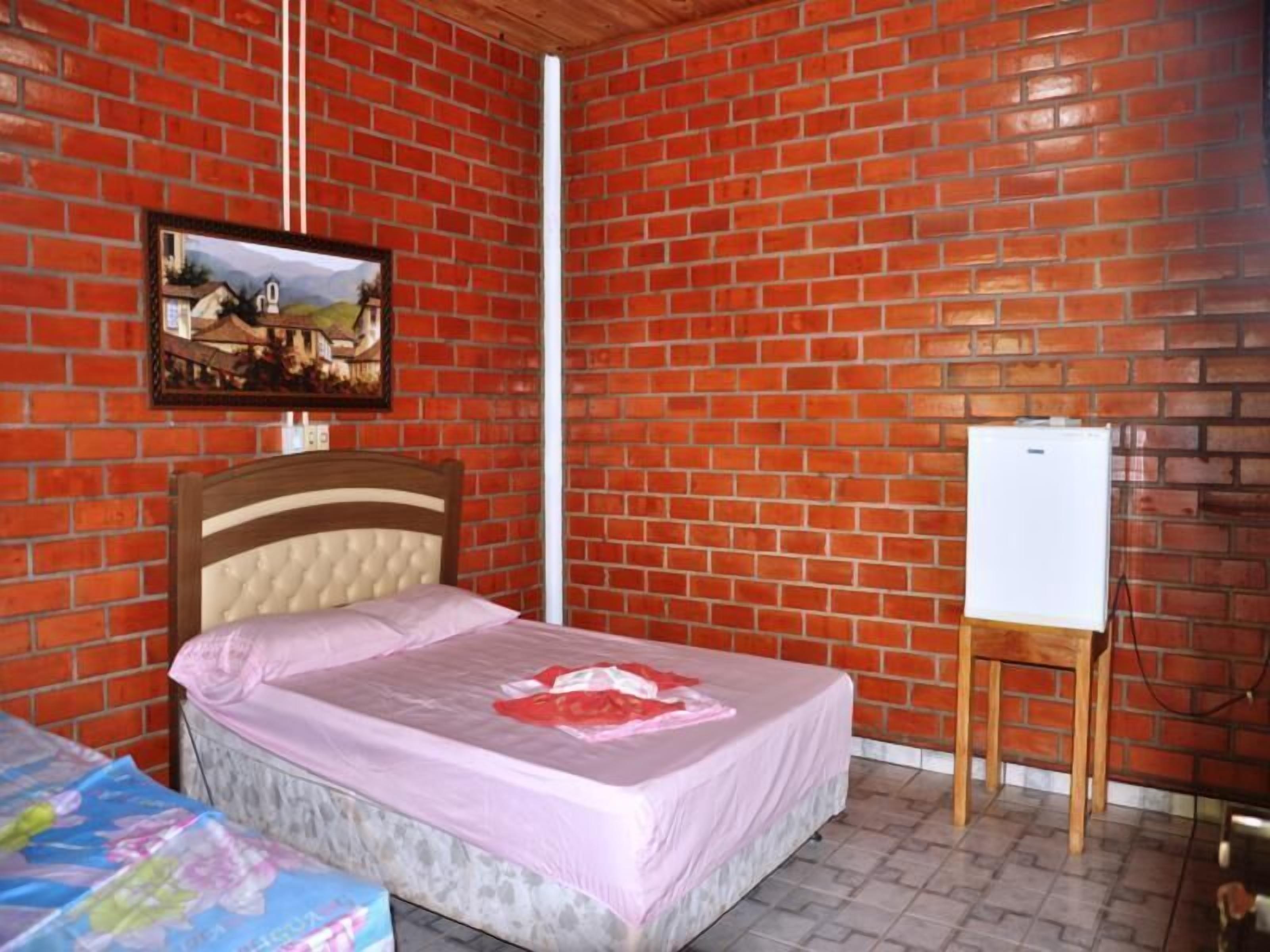 Een kamer met een bakstenen muur, een bed met hoofdeinde, een klein tafeltje en een whiteboard.