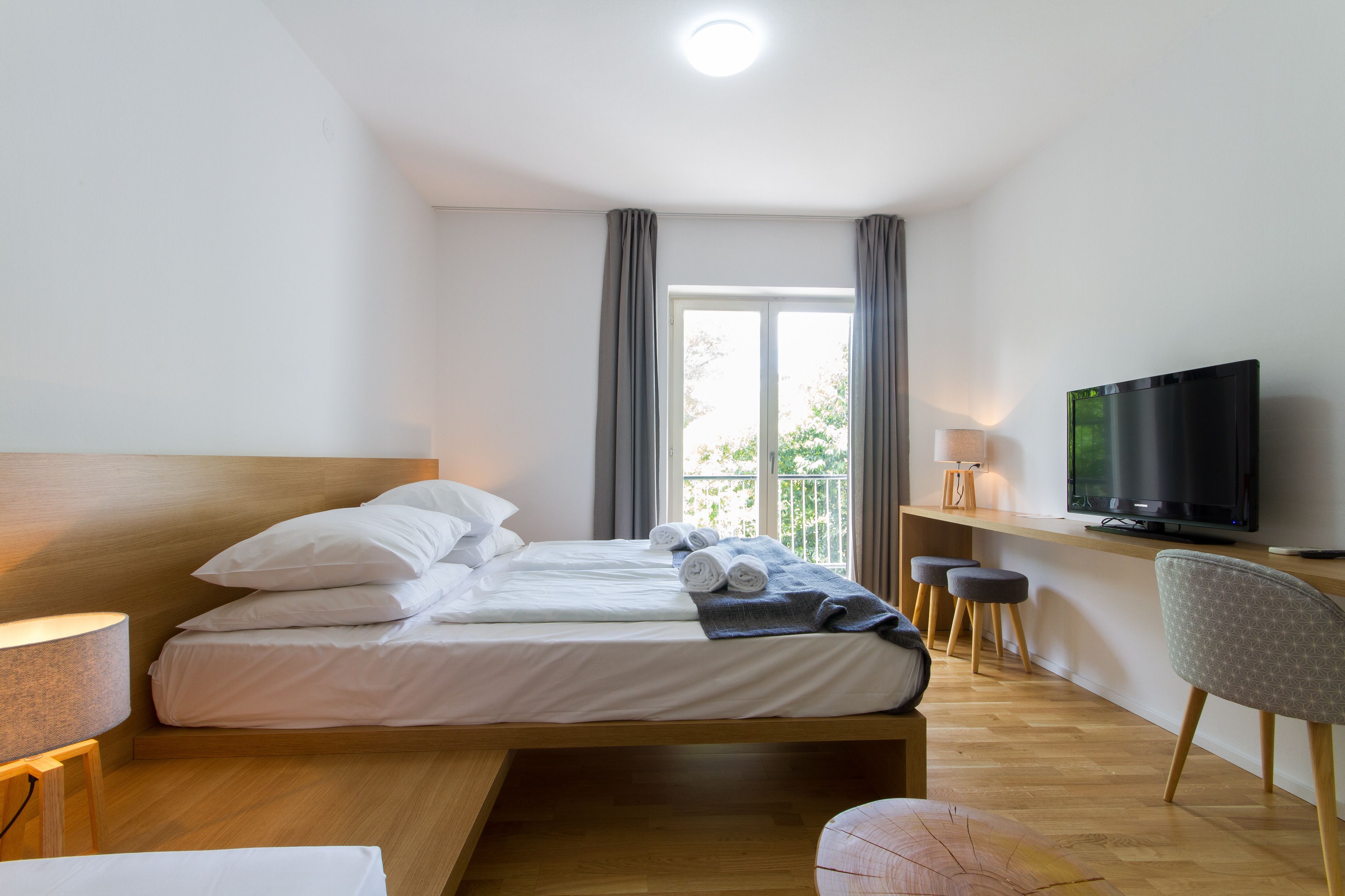 A hotel room with a bed, a TV, a desk, and a window with curtains.