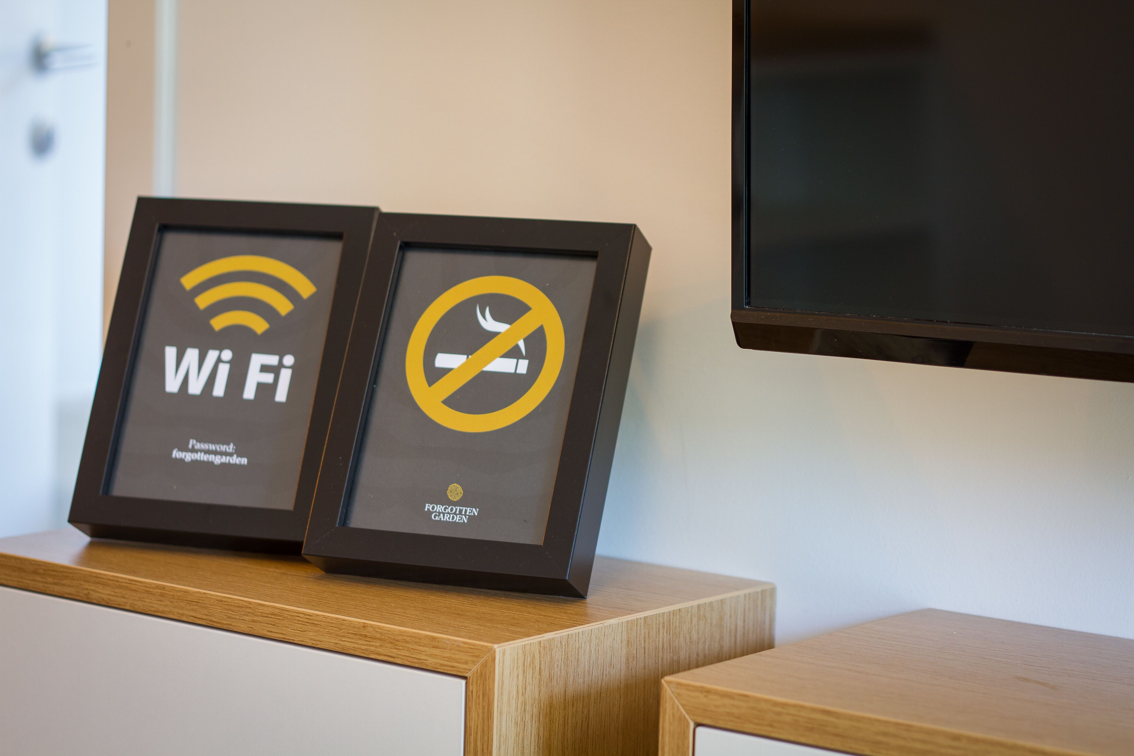 Two framed signs on a wooden surface, one with a Wi-Fi symbol and text, and the other with a no-smoking symbol.