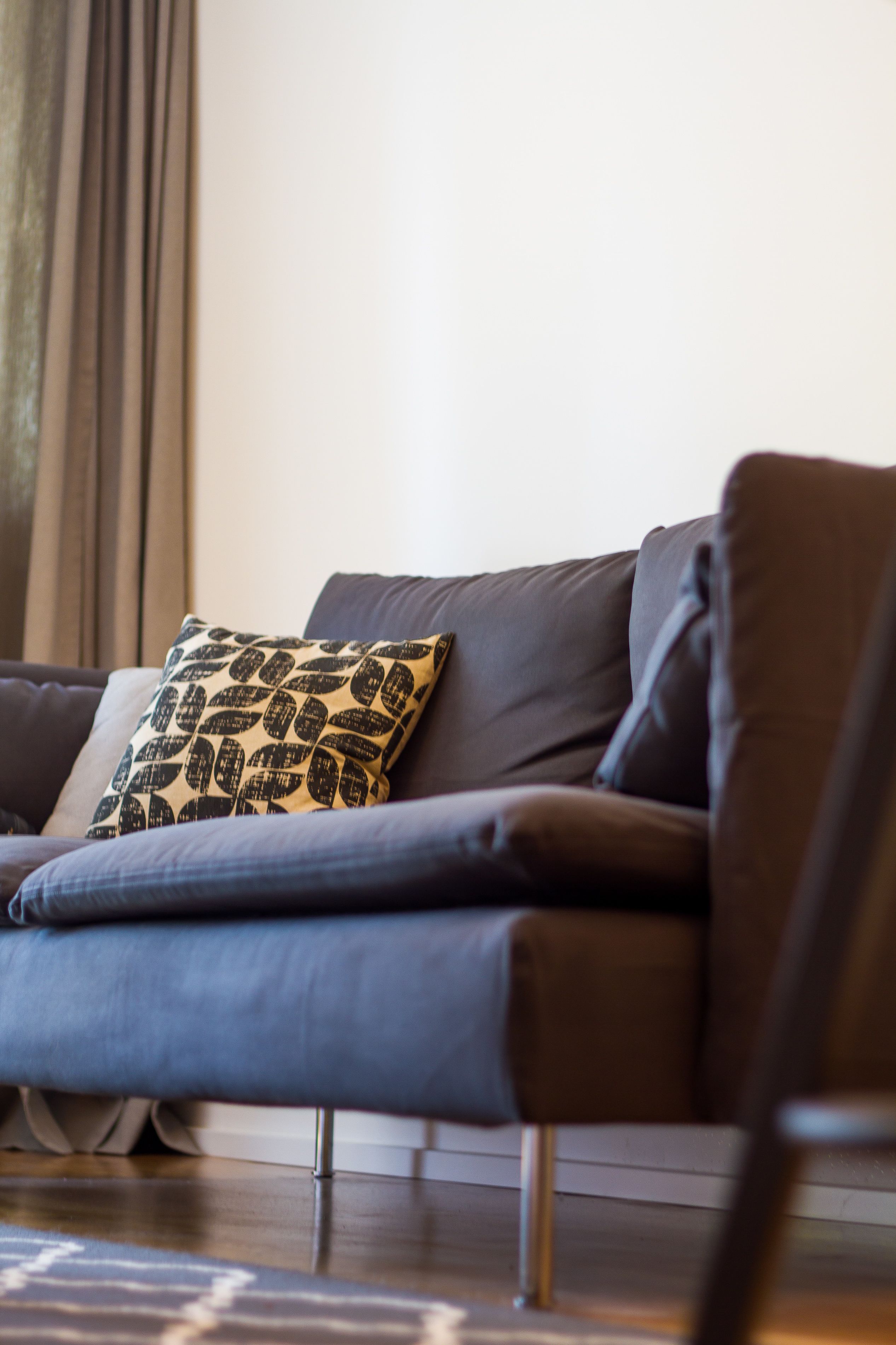 A modern living room with a dark grey sofa, a patterned throw pillow, and a wooden floor.