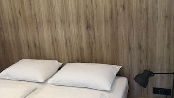 Una cama con ropa de cama y almohadas blancas, una mesita de noche con una lámpara y una pared de madera.
