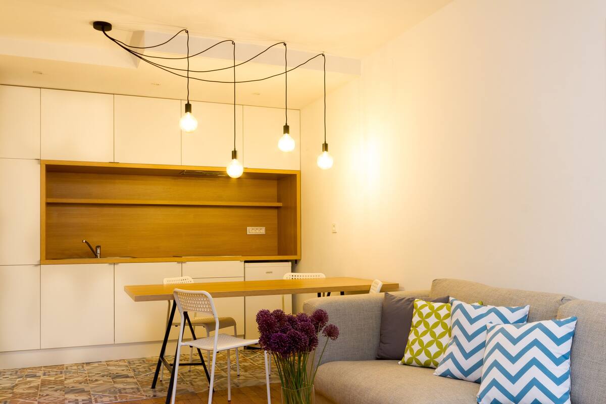 A modern living room with a sofa, a dining table, and a kitchen area with wooden cabinets.