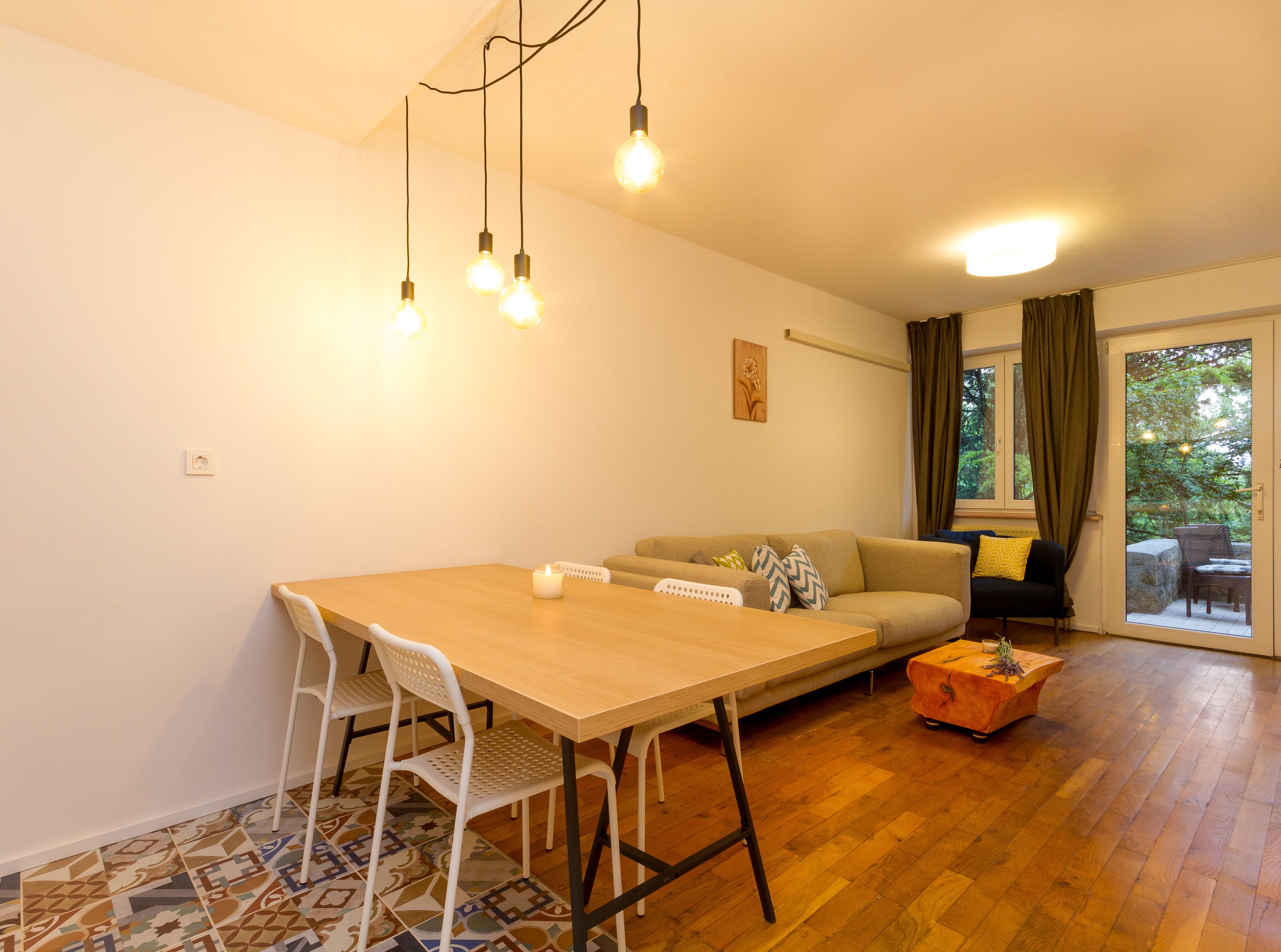 Un comedor con una mesa de madera, sillas blancas, un sofá y un tapete estampado.