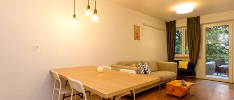 Un comedor con una mesa de madera, sillas blancas, un sofá y un tapete estampado.