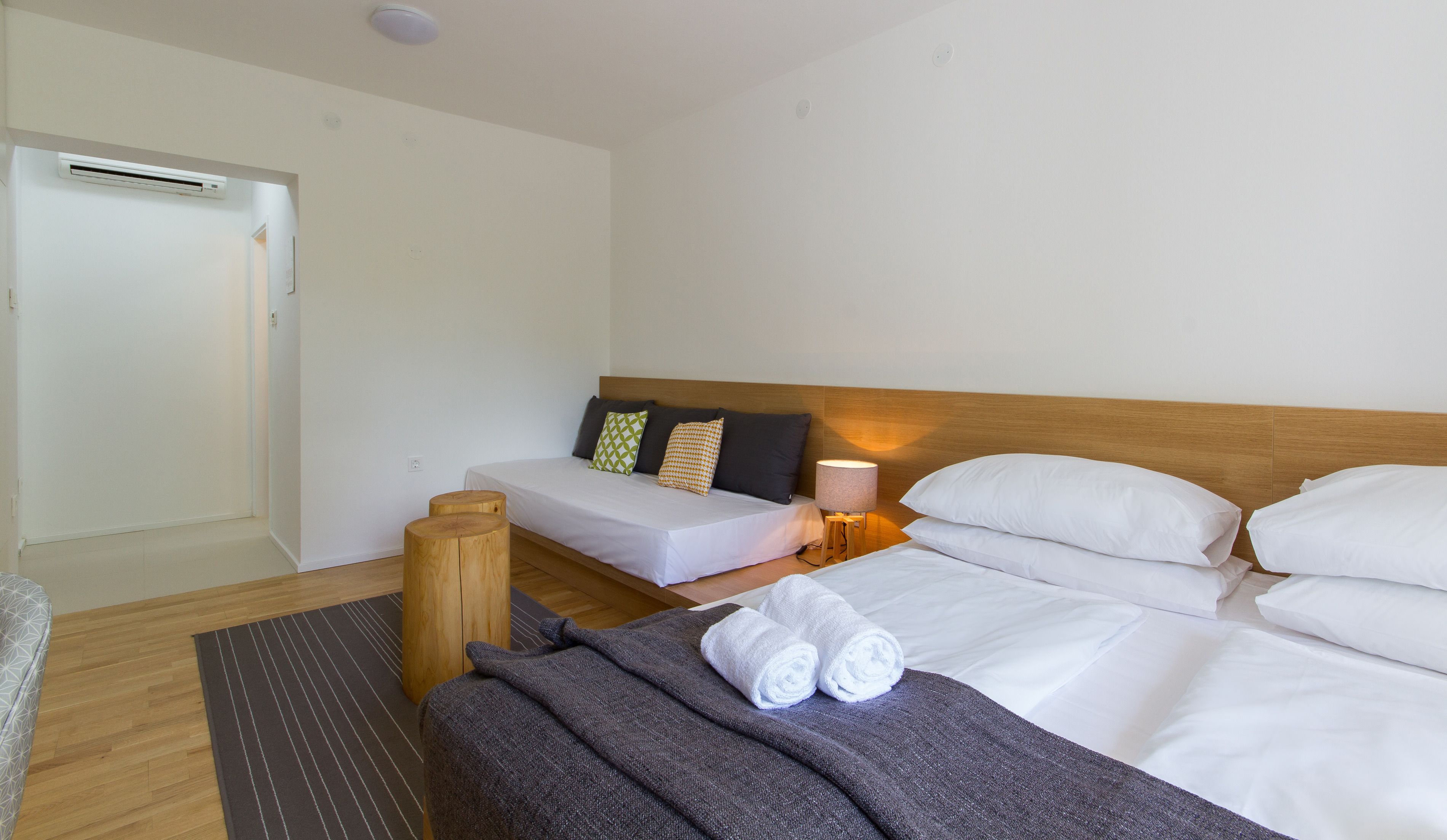 A hotel room with a bed, bedside table, lamp, and a small wooden stool.
