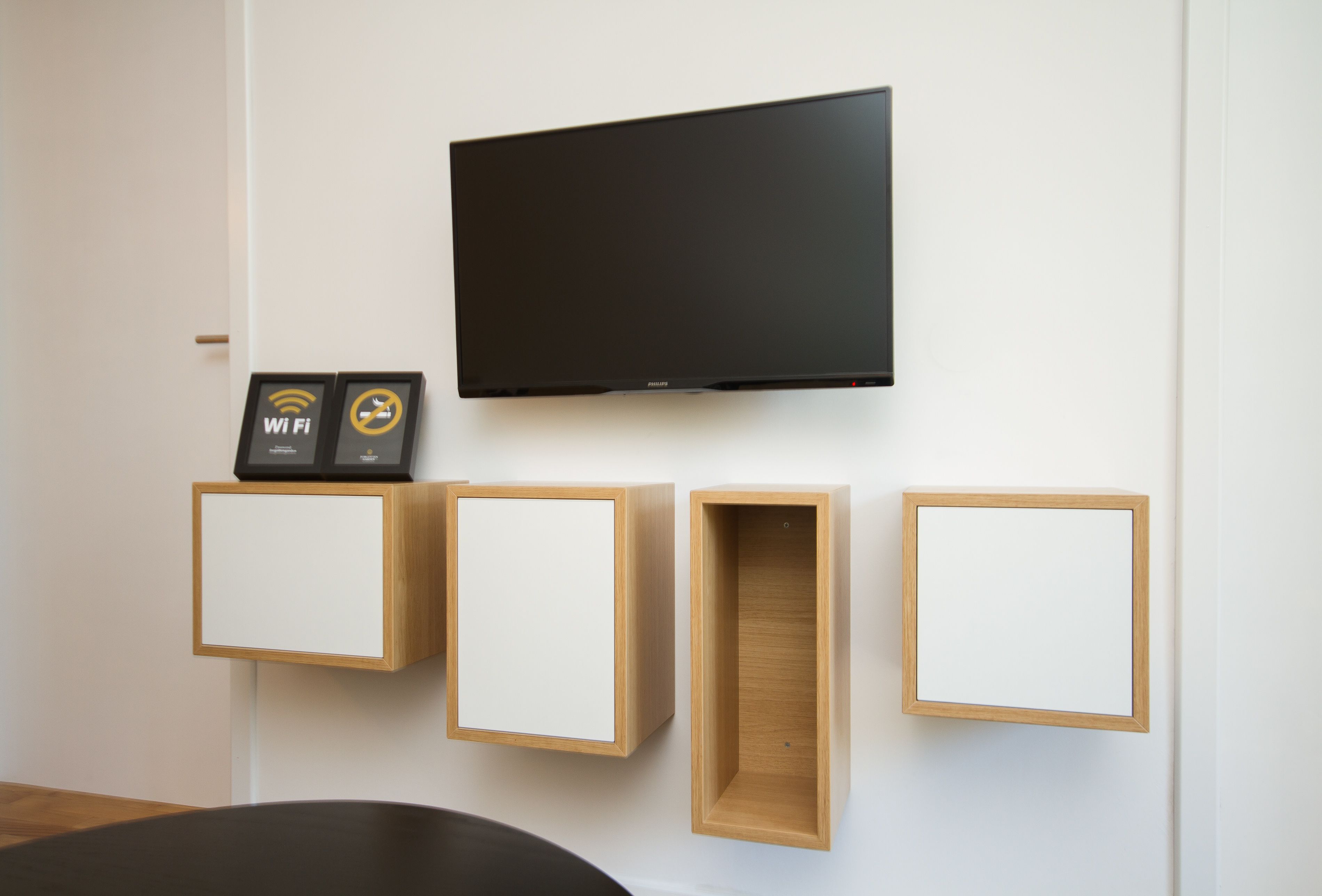 Une chambre moderne équipée d’un téléviseur à écran plat fixé au mur, de meubles en bois fixés au mur et d’un symbole Wi-Fi encadré.