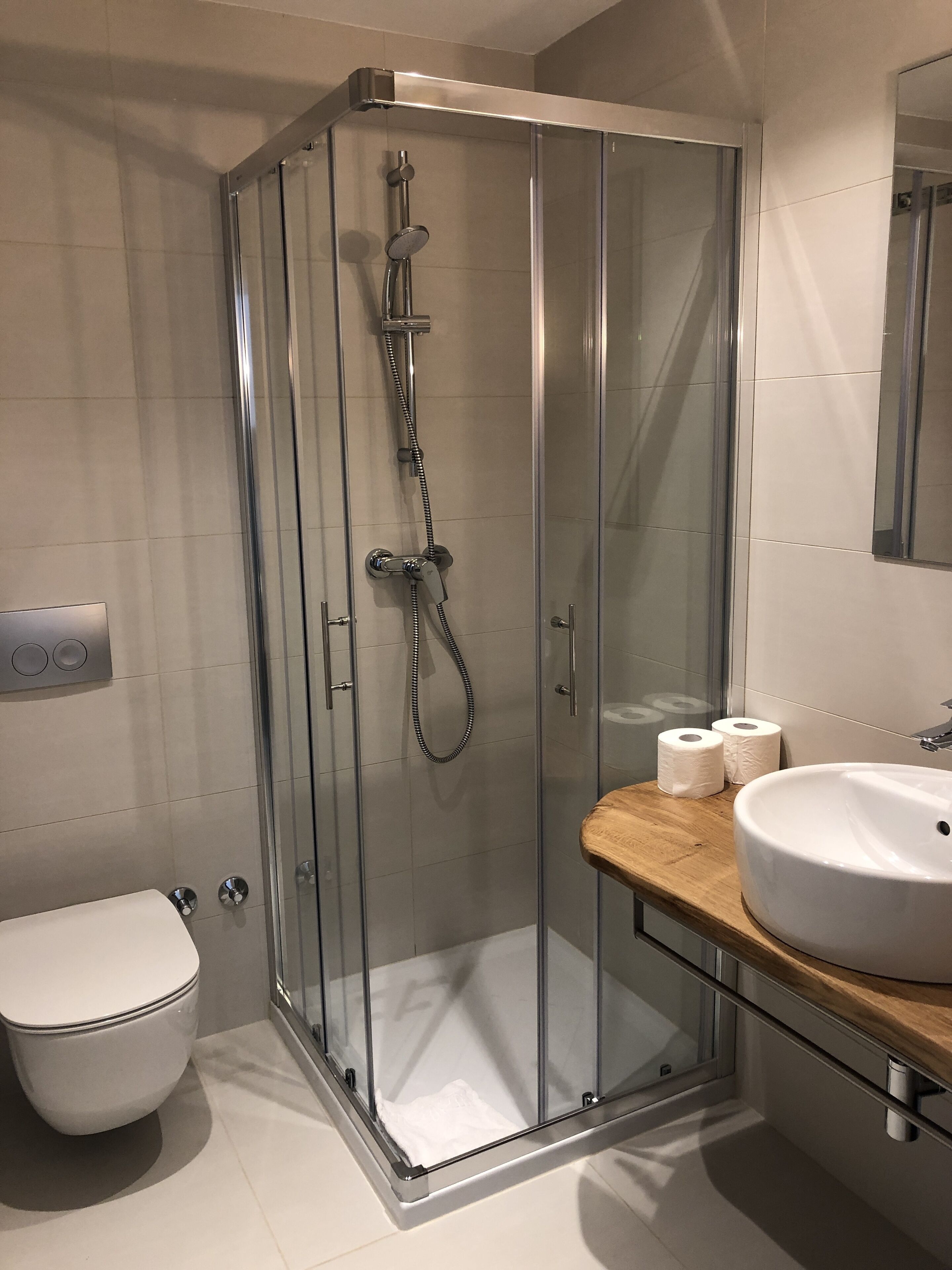 Un bagno moderno con cabina doccia in vetro, un water bianco e un mobile lavabo in legno.