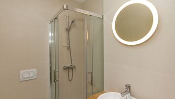 A modern bathroom with a glass-enclosed shower, a round mirror with a light, and a wooden vanity with a sink.