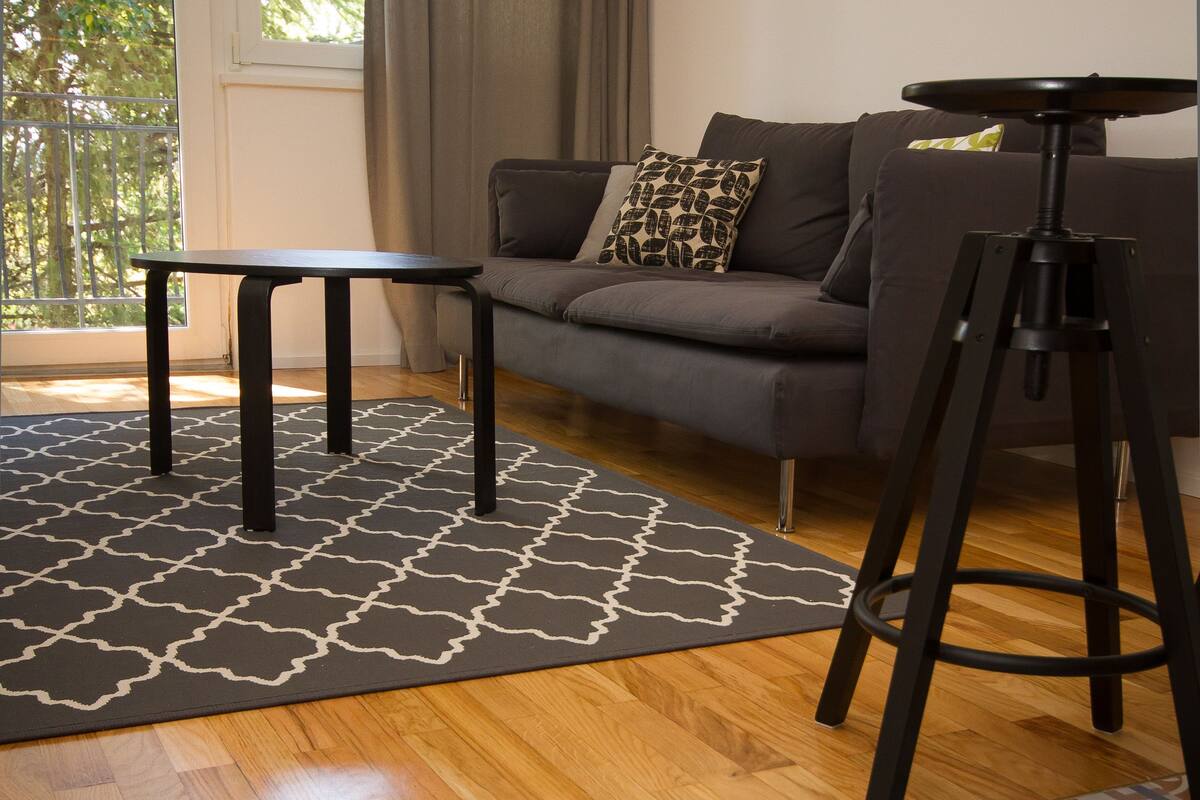 A modern living room with a grey sofa, a black coffee table, and a tripod.