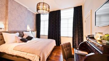 Een slaapkamer met een groot bed, een bureau, een stoel, een kroonluchter en een raam met gordijnen.