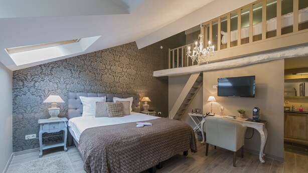 A bedroom with a bed, bedside tables, a desk, a chair, a TV, and a staircase leading to an upper level.