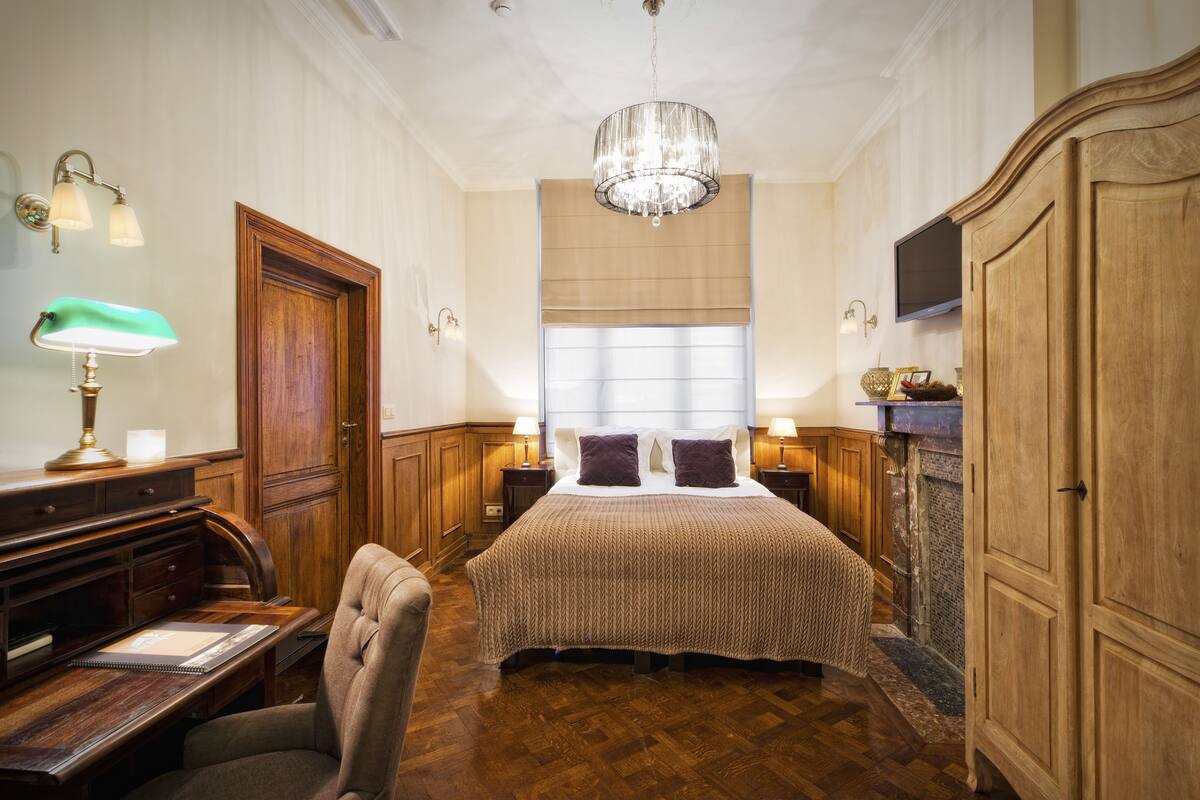 Une chambre à coucher avec un grand lit, une armoire en bois, un bureau et un lustre.
