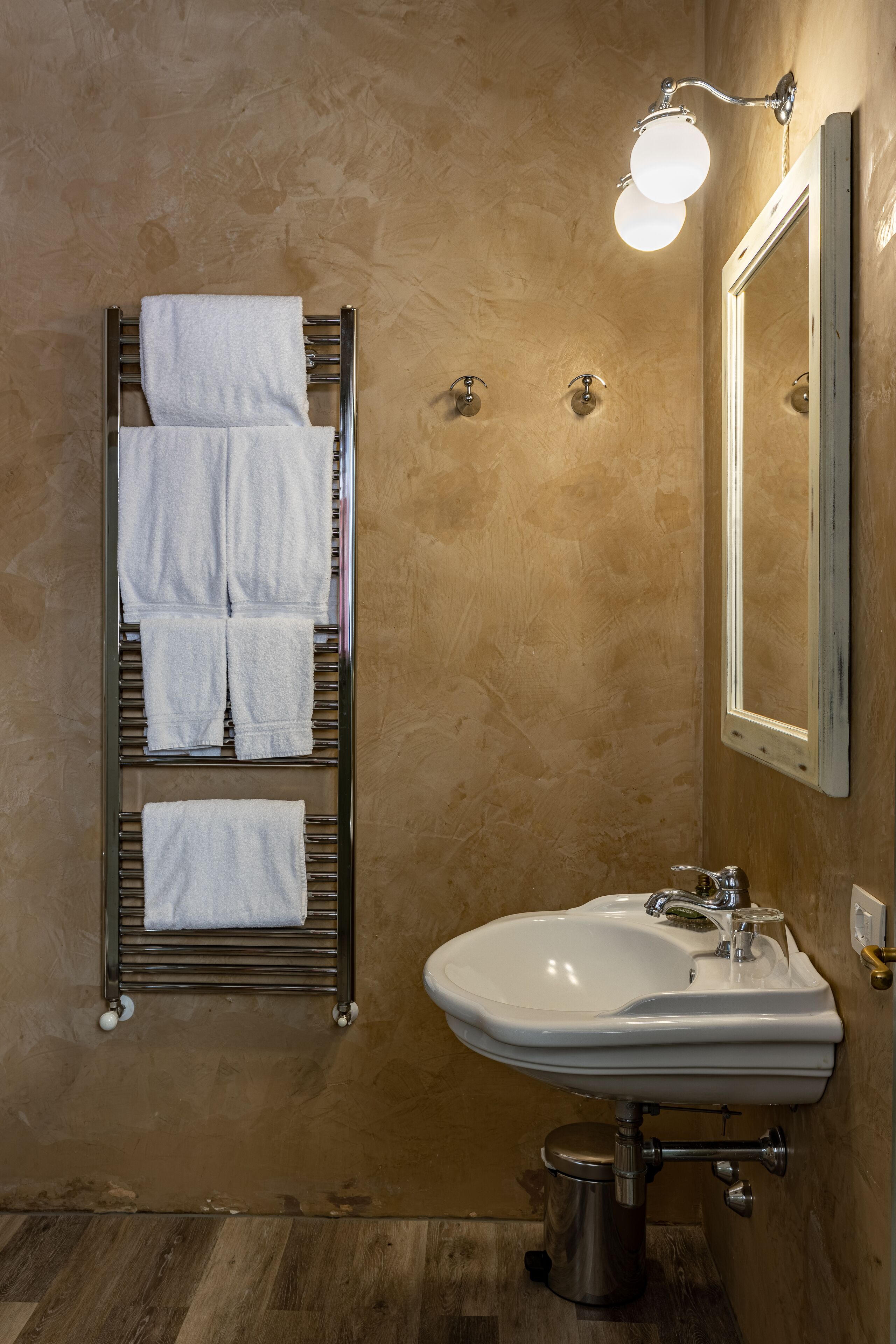 A bathroom with a towel rack holding four towels, a white sink, and a mirror.