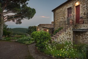 A stone building with a stone staircase, surrounded by lush greenery and a stone pathway. - Le Ragnaie (Montalcino)