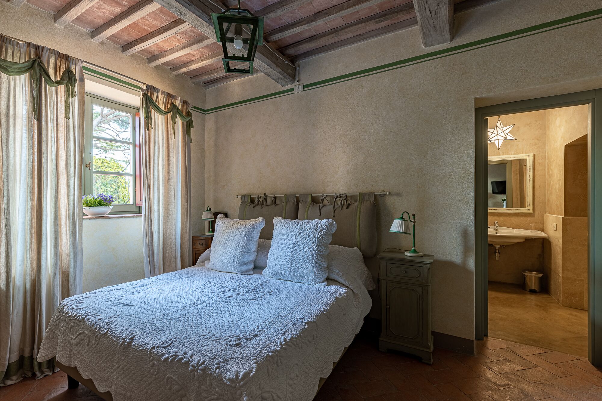 Quarto com cama grande, mesa de cabeceira, penteadeira e banheiro visível por uma porta aberta.