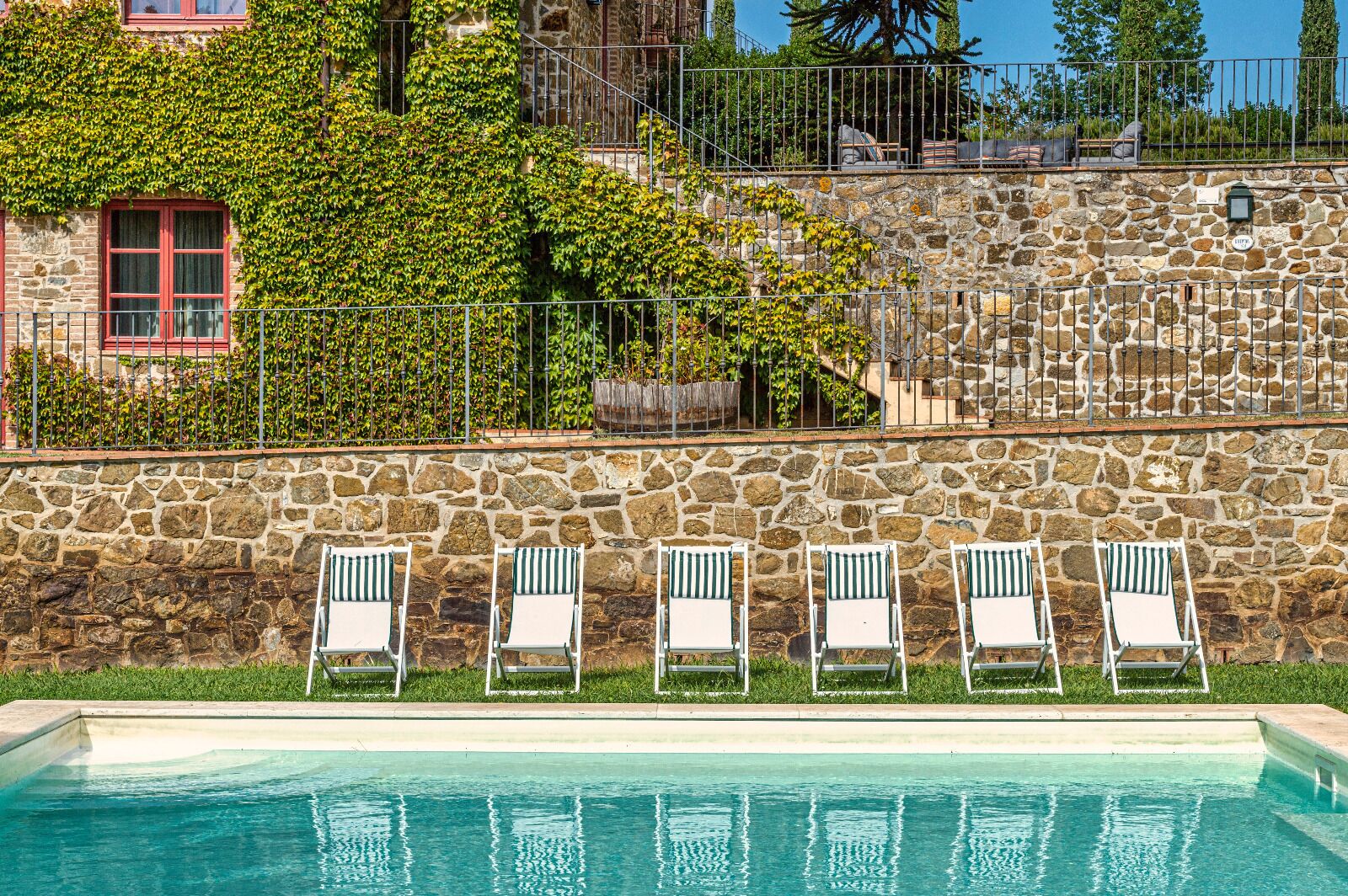 Un muro de piedra con piscina y sillas de descanso.
