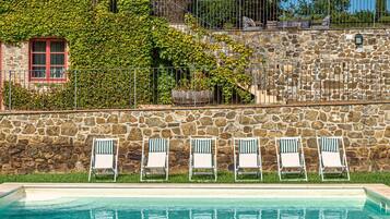 Un muro de piedra con piscina y sillas de descanso.