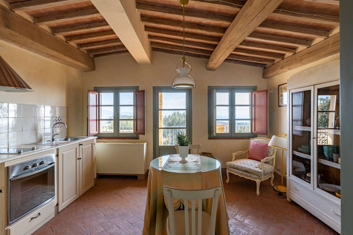 A kitchen with wooden beams, a dining table with chairs, a cabinet, and a window with a view.