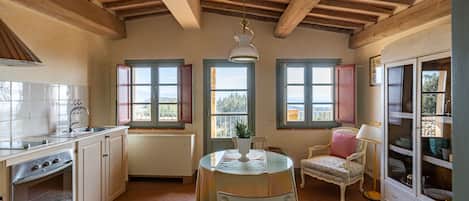 A kitchen with wooden beams, a dining table with chairs, a cabinet, and a window with a view.