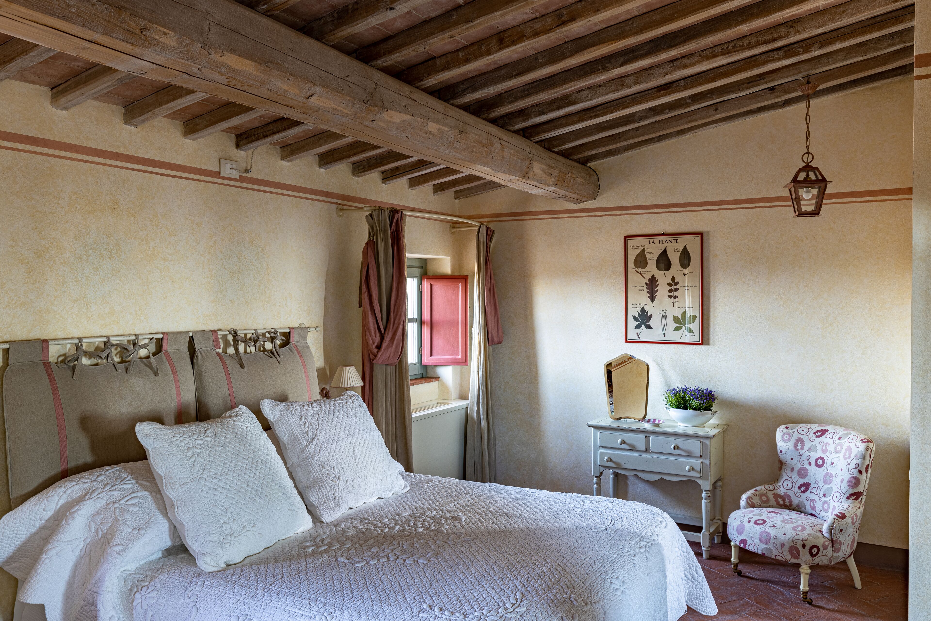 A bedroom with a large bed, a nightstand, a chair, and a wall-mounted mirror.